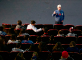 Liceales en botacas del cine y docente hablando al frente