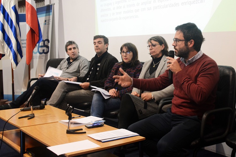 Expositores sentados, hombre hablando con micrófono en mano