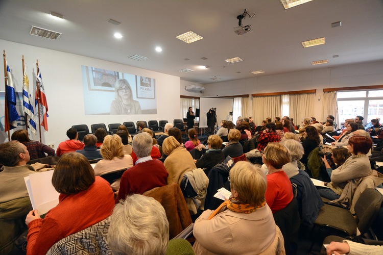 Auditorio con público sentado y se proyecta en video el saludos de la Directora Nacional de Educación Rosita Angelo